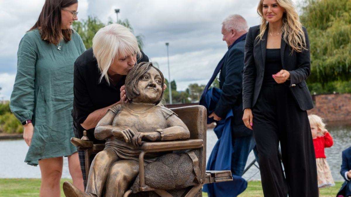 The Remembering Stella Young statue is unveiled. Lynne, Stella&rsquo;s Mum, kisses the head of the statue, as the Young family is gathered behind.