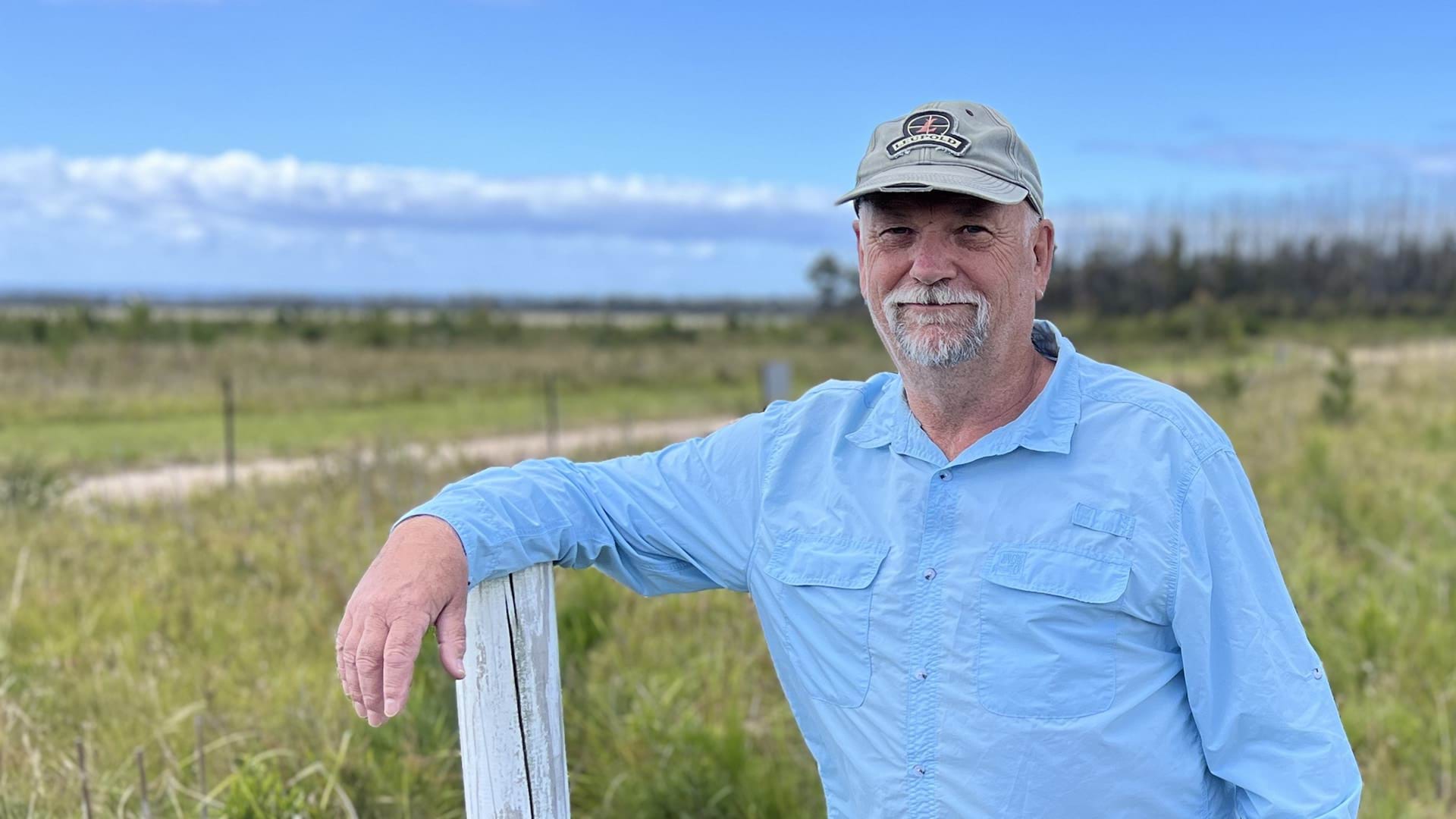 Mallacoota Gun Club, Treasurer, Dave Whittle wearing a blue shirt and leaning on a fence post in an outdoor field setting