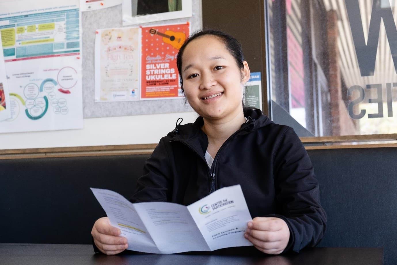 Paw Say Paw portrait, seated at a table, holding a brochure.