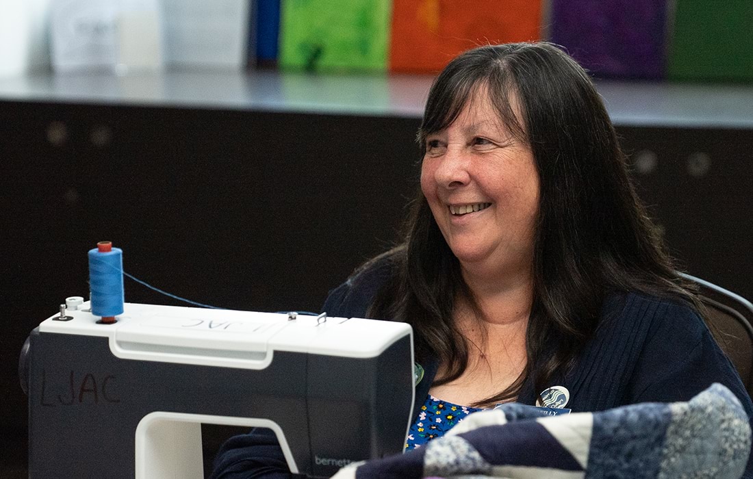 A lady with black hair sitting in front of a sewing machine